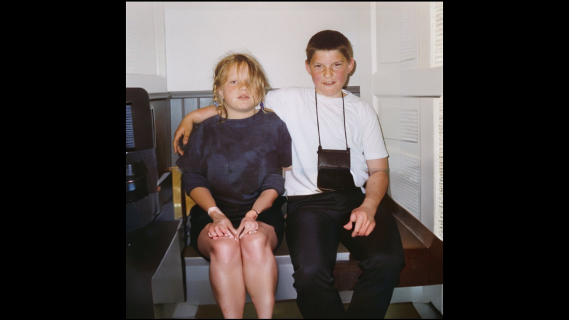 Childhood photograph: two children sit side by side on a bench, one with an arm around the other. CyberCindy (2025) by Nickii Schamborski.
