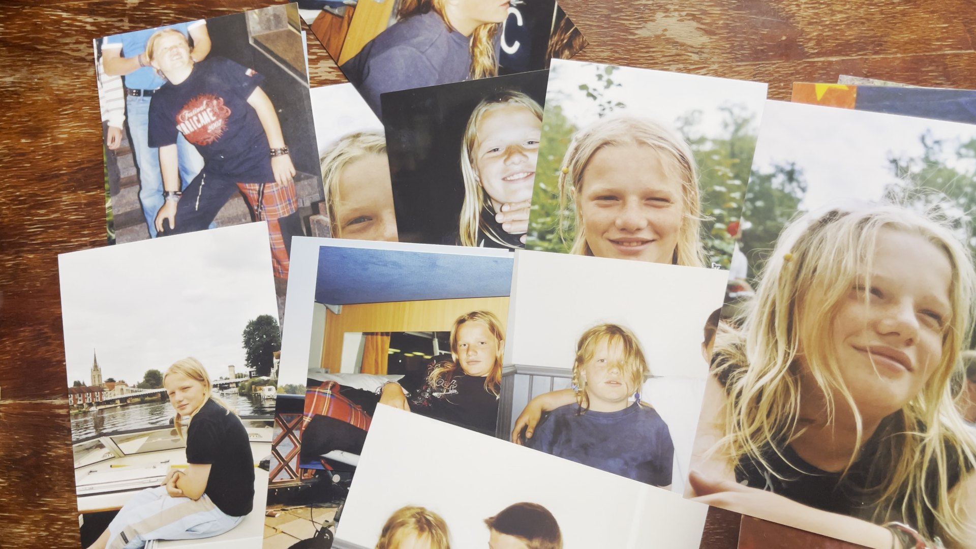 Printed childhood photographs of a blond child spread out on a wooden table. CyberCindy (2025) by Nickii Schamborski.