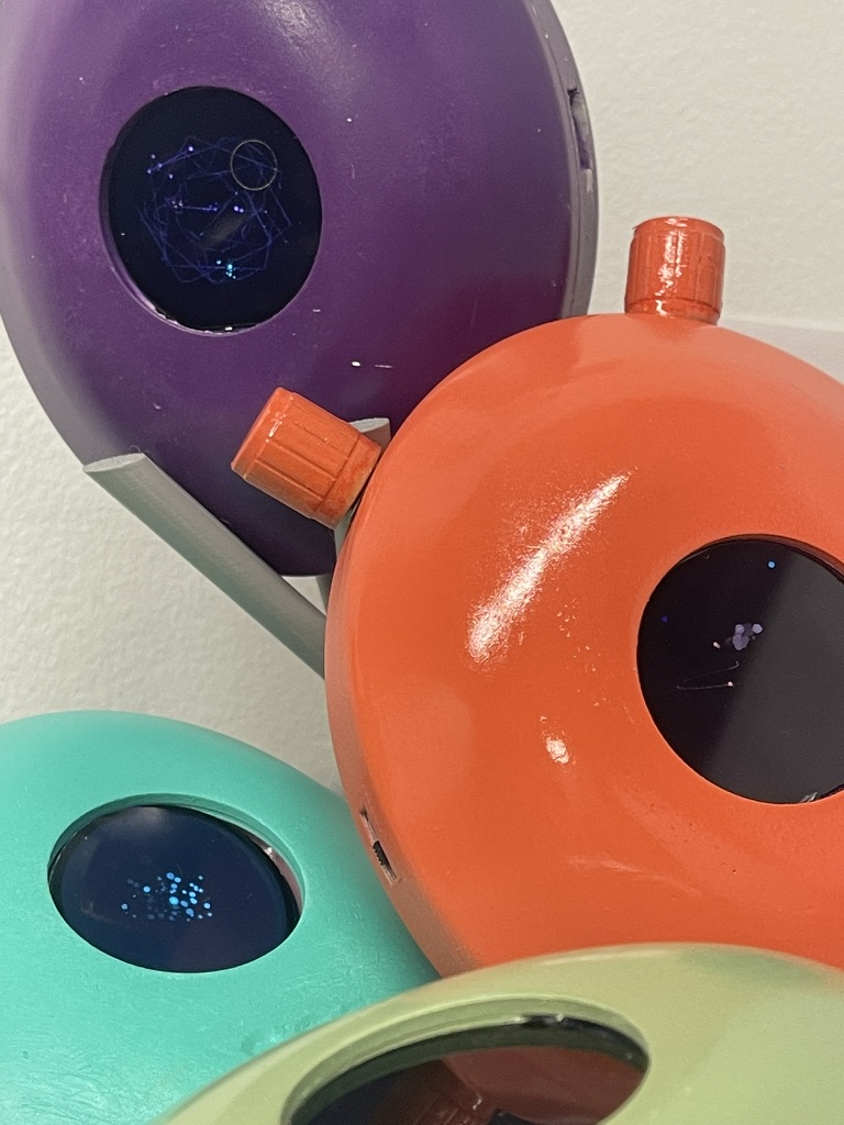 Close-up of glossy purple, orange, mint and green disc-shaped devices, each with a dark round display. Funke (2026) by Nickii Schamborski.