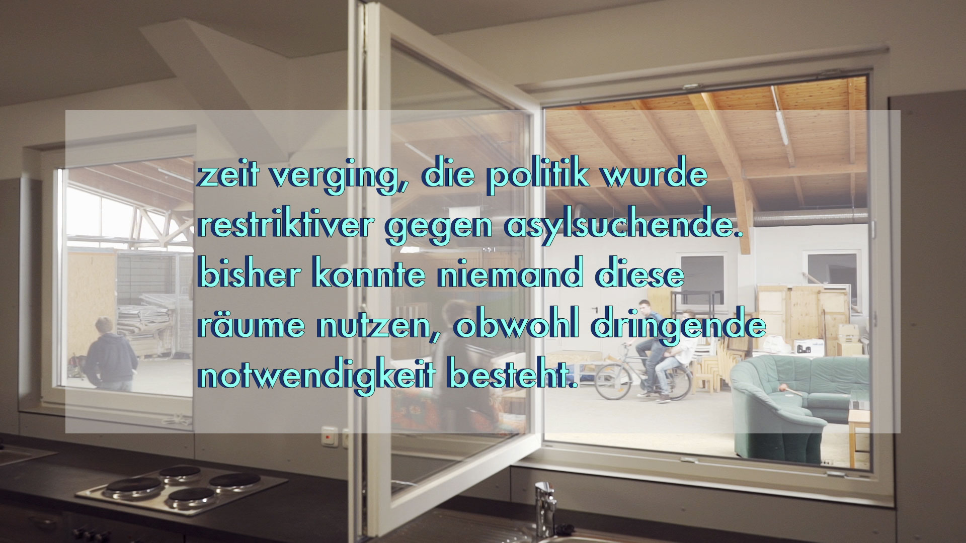 Video still: view through an open window from a kitchen into a hall with stored furniture where a person rides a bicycle; overlaid German text says that asylum policy became more restrictive while these rooms stayed unused. Unused Capacity (2018) by Nickii Schamborski.